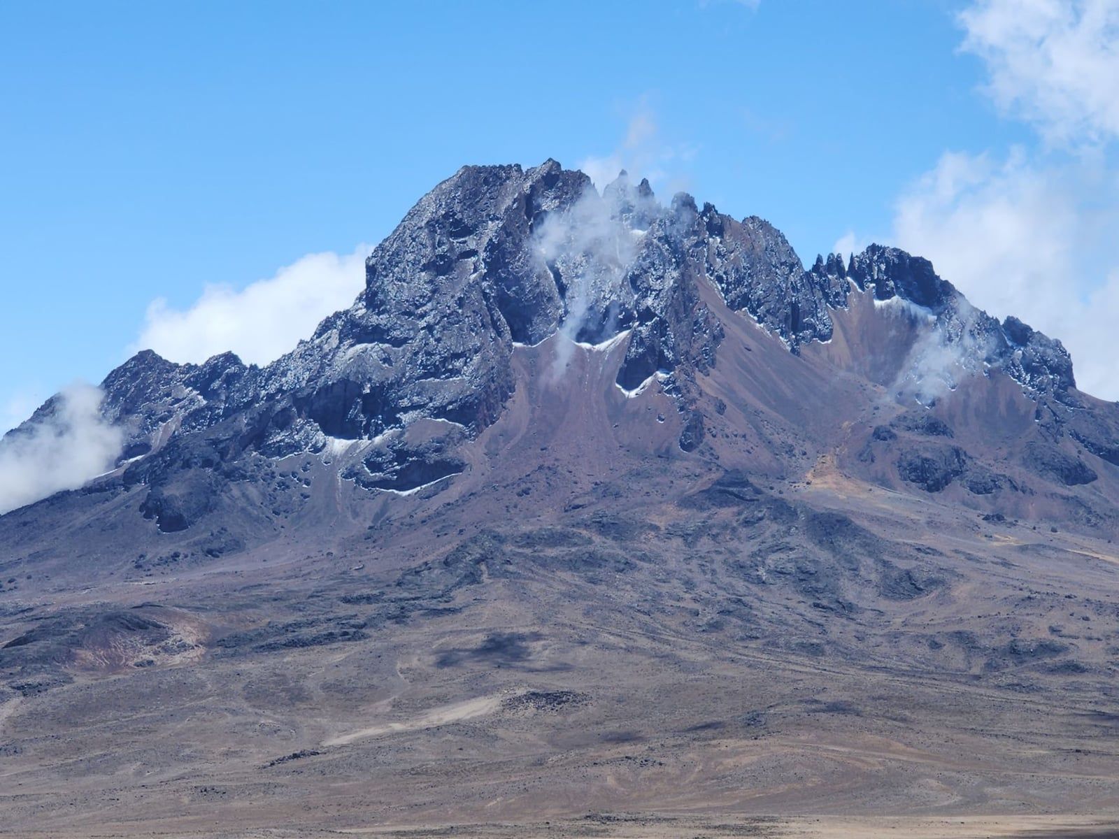Rugged, craggy slopes and rocky summit towers of Mawenzi Peak on Mount Kilimanjaro against a blue sky.